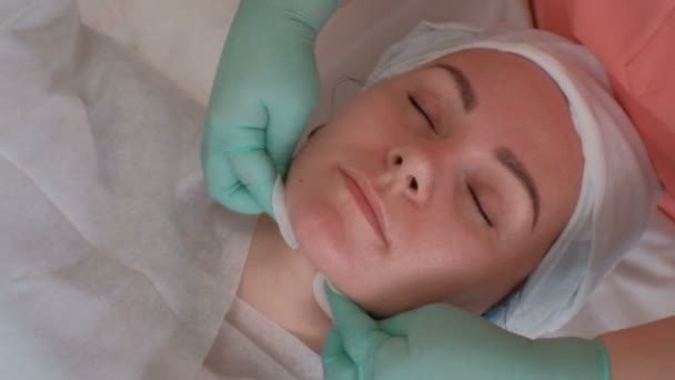 青い手袋で美容師は 綿のパッドを持つ若い女性の顔をこすり 美少女ソフトの手順 回復と女性の肌の若返りの手順 — ストック動画