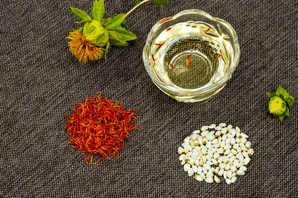 Safflower. Oil, seeds, bud, flower, red inflorescences of wild saffron. Close-up, Gray woven background. Ingredients for health, cosmetology and paint