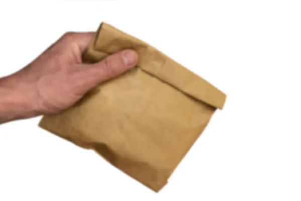 Wazig. Mannenhand houdt een bruine papieren zak met inhoud. Geïsoleerd op een witte achtergrond. Kopieer ruimte. Het thema van het gebruik van milieuvriendelijke verpakking. — Stockfoto