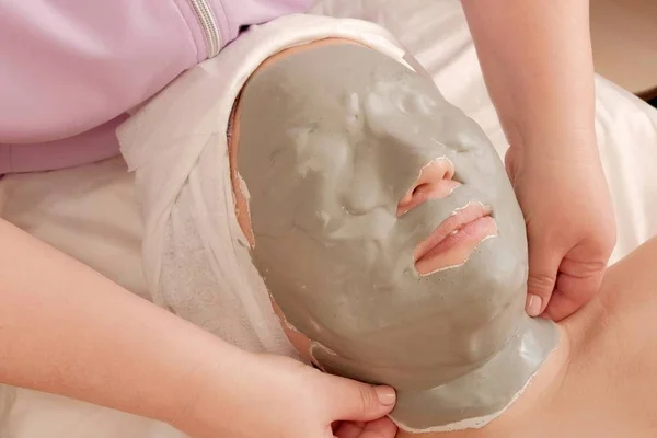 Een vrouw is liggend op een bank met een alginaat masker op haar gezicht in een schoonheidssalon. Gezondheid en kalmerende vrouwelijke huid cosmetische procedure in de schoonheidssalon. — Stockfoto