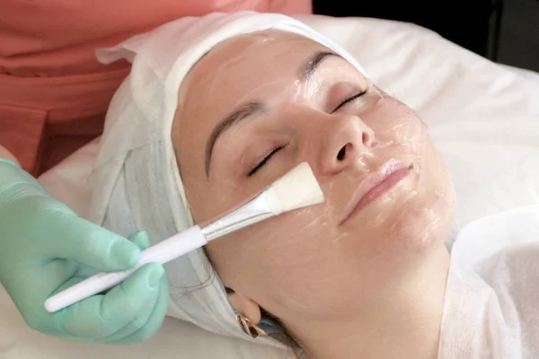 De procedure voor de toepassing van een gezichtsmasker in de schoonheidssalon. Schoonheidsspecialist handschoenen uitstrijkjes borstel gel op van het meisje gezicht. Cosmetologie. Schoonheid — Stockfoto