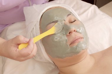 Beautician apply alginate mask with algae on the girl's eyes. Rejuvenating treatment in the beauty salon. Cosmetic care for face and body clipart