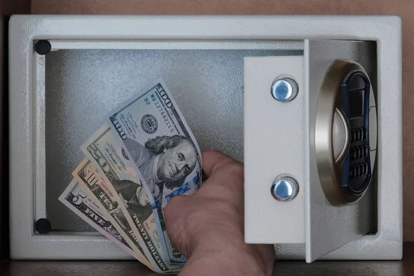 Close-up of a man's hand putting American dollars in a safe Deposit box. Banknotes of 5, 10, 20, 100 US dollar. Storage of money, stocks and jewelry in a Bank Cabinet. — Stock Photo, Image