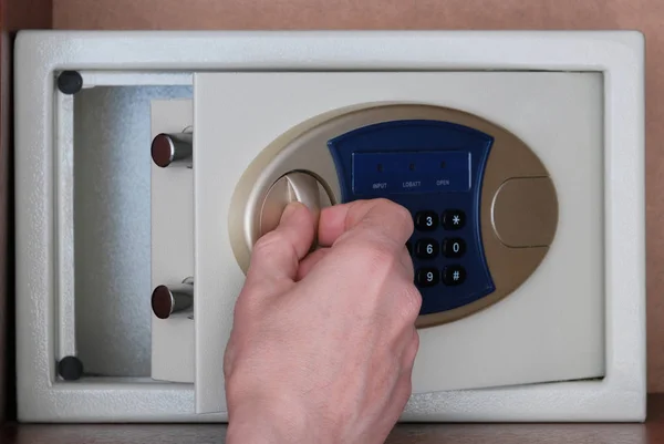 The man opened the safe hidden in the office in the closet to put the money. Close-up of the hand opening the door. Safety of precious things in a safe with a combination lock. Secure Bank code