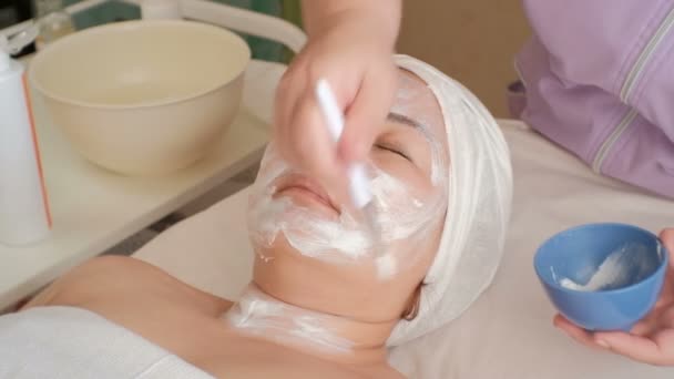 一个亚洲女孩在美容院的脸 美容师用刷子将白色按摩霜涂在穆斯林妇女的颈部区域 美容手术清洁和恢复皮肤活力 — 图库视频影像