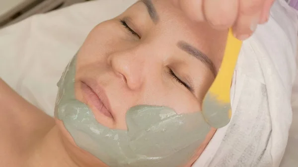 Zbliżenie kosmetyczki stawia alginian maski z zielonych alg na twarzy azjatyckich dziewcząt. Maska z efektem podnoszenia dla kobiet. Zabieg kosmetyczny do pielęgnacji twarzy. — Zdjęcie stockowe