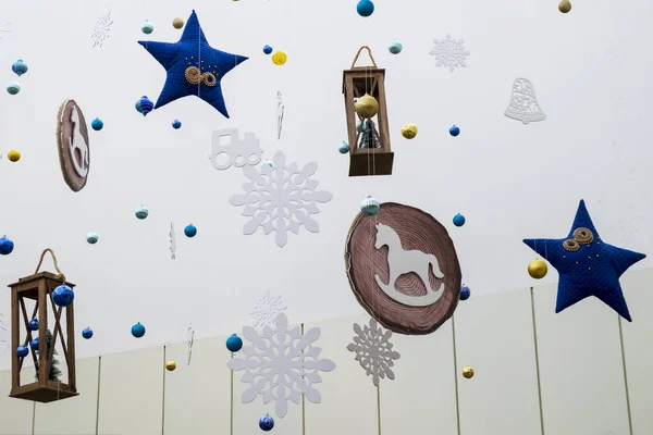 Festlig dekoration av rummet i Nyårs stil. Blå stjärnor, snöflingor, lyktor, hästar, klockor och andra leksaker hänger på tunna trådar på en vit bakgrund. Jul koncept för korten. — Stockfoto