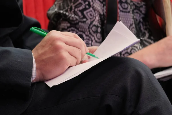 Close-up da mão de um homem escrevendo em papel com uma caneta verde. Um homem adulto registra informações durante uma reunião no escritório . — Fotografia de Stock