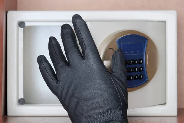 Theft of valuables and money. A black-gloved thief opens the safe door with a combination lock. Security at home, hotel and office