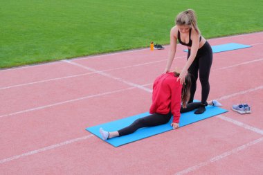Kırmızı kazaklı genç kızlar esneme hareketleri yapıyorlar. Koç, partnerini sicimin üzerine gerer. Parktaki dersler. Sağlığa. Esniyorum..