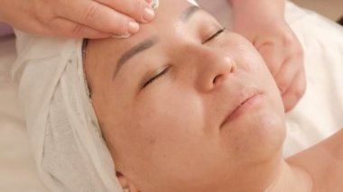Kozmetolojist bir güzellik salonunda Asyalı bir orta yaşlı kadının yüzünün deri temizler. Kızlar için kozmetik prosedür. Gençleştirme ve iyileşme.