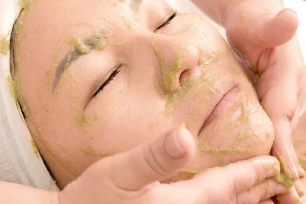 美容師は、アジアの女の子の顔に緑のマスクを置きます。キウイの種のマスクで女性の顔のクローズアップ。美容。美しさ。人の健康. — ストック写真