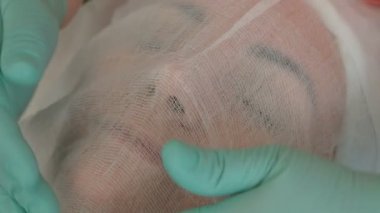 Yeşil eldivenli bir kozmetolojistin elleri bir kadının yüzünde gazlı bezle kaplıdır. Güzel bir kız bir güzellik salonunda bir prosedür üzerindedir. Aljinat maskesi uygulamak için hazırlık prosedürü.