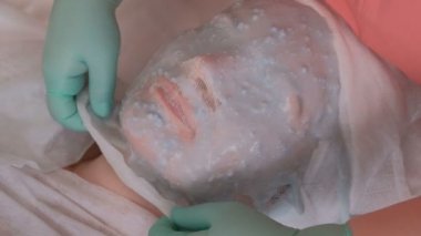 Güzellik uzmanı bir kadının yüzündeki aljinat maskesini temizler. Güzellik salonunda prosedür üzerinde güzel kız. Besleyici mavi kozmetik maske.