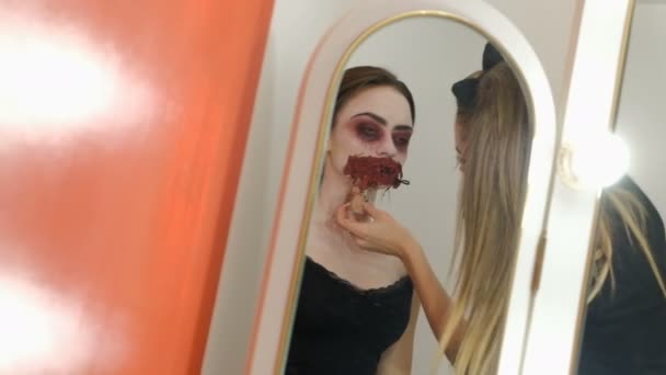 ハロウィーンを祝うために怖いメイク 口を縫い上げた少女 鏡の反射 美少女は女性の顔の血まみれの塗料を塗ります すべての聖人の日や邪悪なパーティーのためのカーニバルへのコスプレ — ストック動画