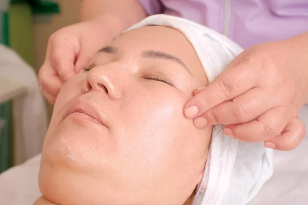 Aziatische vrouw zittend in een stoel bij de masseur. De arts doet een gezichtsmassage van rimpels voor het meisje in de Spa. Hijs effect. Huidverzorging — Stockfoto