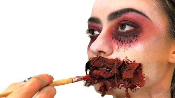 Närbild av flickans ansikte med en skrämmande mask för Halloween eller alla helgons dag. Stylist ritar en skrämmande makeup för modellen. Förberedelser inför semestern. — Stockfoto