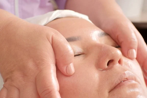 Close-up massage van een Aziatisch vrouwtje. Gladmakende rimpels op het gezicht van de vrouw. Gezichts-en lichaamsverzorging in de schoonheidssalon. — Stockfoto