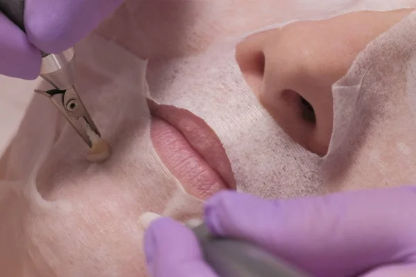 Close-up. De handen van een cosmetoloog in Lila Handschoenen houden de elektroden op de kin van een vrouw. Microcurrent gezichtsmassage. Gezondheid en schoonheid. Vrouw van middelbare leeftijd in een schoonheidssalon. Cosmetische procedure. — Stockfoto