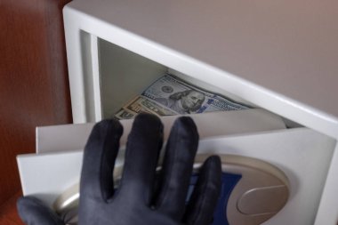 Siyah eldivenli sağ el kasa kapısını açar. Kasadan dolar hırsızlığı. Ofis, otel veya evde paranın korunması ve güvenliği kavramı.
