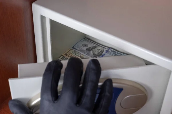 The black-gloved right hand opens the safe deposit box door. Theft of dollars from the safe. Concept of protection and security of money in the office, hotel or home. — Stock Photo, Image