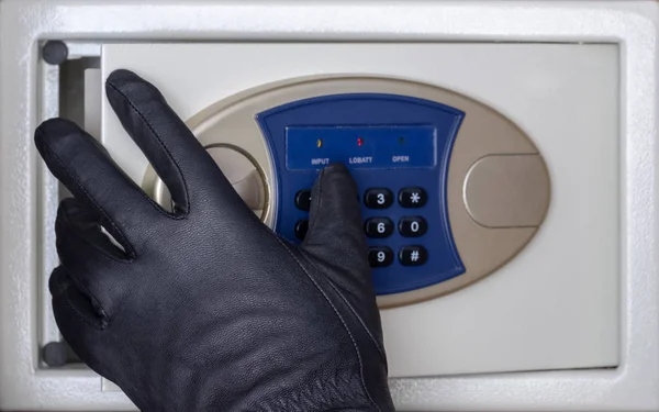 A black-gloved thief opens the safe door with a combination lock. Security at home, hotel and office. Concept. Theft of valuables and money.