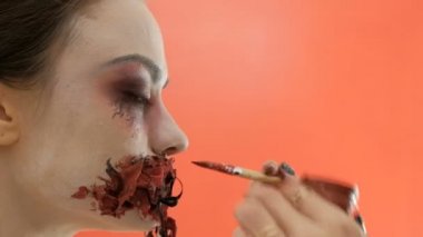 Cadılar Bayramı kutlaması için makyaj. Bir makyaj sanatçısının elinde fırça. Kız kırmızı bir boya kanlı ağız çizer. Uğursuz bir partide korkunç bir bayan bir görüntü.