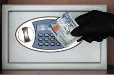 Siyah bir eldiven bir kombinasyon kilidi ile bir kasa önünde Amerikan doları bir tomar tutar. Para ve mücevheri hırsızlıktan koruma kavramı. Parayı güvenli bir yerde tutmak