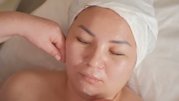 Demonstração de alterações na face feminina após um procedimento cosmético. As mãos de um terapeuta de massagem esteticista gastam no queixo, bochechas e sobrancelhas de uma menina asiática. Elevação e limpeza da pele . — Vídeo de Stock
