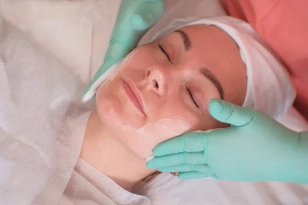 La chica pasa por tratamientos faciales en el salón de belleza. El esteticista que usa guantes aplica crema hidratante en la cara de la mujer. Faciales en el Spa —  Fotos de Stock