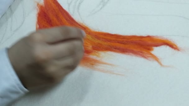 Close-up. Um adolescente com uma camisa branca coloca uma agulha sobre um feltro seco alaranjado. Fazendo um quadro de lã colorida em uma base de tecido branco. Artesanato . — Vídeo de Stock