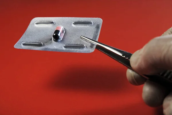 Az egyetlen tabletta a buborékfólia egy piros háttér. A kéz egy orvosi kesztyűben tart a tabletta csipesszel. Térmásolat. A választék, a betegség és a kezelés, az orvostudomány és az egészségügy fogalma. — Stock Fotó