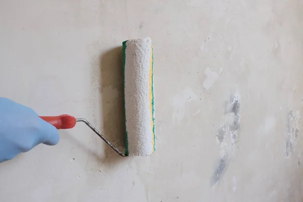 Mavi eldivenli bir el, işi bitirmek için bir silindir tutar. Beyaz duvarı astarlama işlemi. Binaların onarımı, inşaat işleri, boyama için oda hazırlama kavramı. Copyspace
