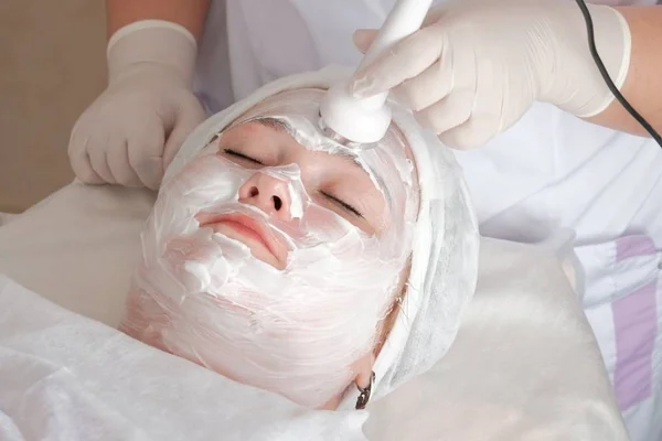 Kosmetyka sprzętowa. Mikroprądowe masaże twarzy. Gruba kobieta na zabieg w centrum kosmetologii. Kosmetyczka w białych rękawiczkach trzymając elektrodę aparatu do masażu. — Zdjęcie stockowe