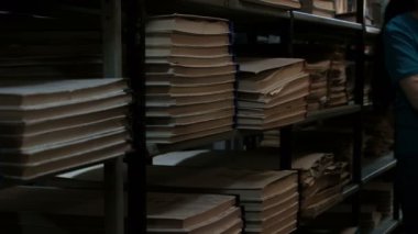 Bodrumda arşiv odası veya kitap deposu. Eski edebiyatlı kitaprafları. Mavi tişörtlü bir kadın gelir ve ışıkları kapatır..