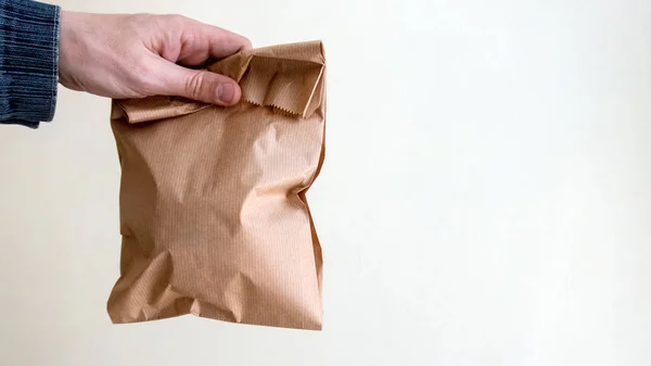 Say no to plastic bags, use paper packaging. Man holding a brown paper bag with contents in his hand. Ecological concept. Copy space. White background.