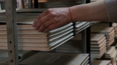 Bir kadın kütüphane rafından büyük bir kitap ya da gazete seti çıkarır. Bir kütüphanecinin eli yakın. Okula geri dön. Eğitim ve öğretim.