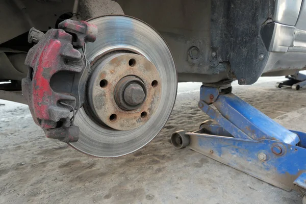 Vecchia macchina sporca issata su un cric. Primo piano di un passaruota senza ruota. Installazione o riparazione di pneumatici del sistema frenante dell'auto . — Foto Stock