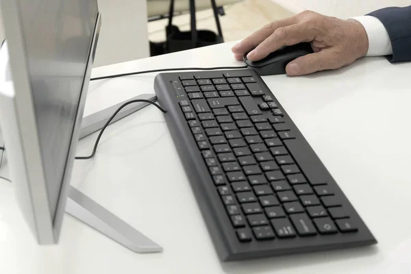 男性の手は、キーボードの横にマウスを保持し、白いテーブルの上にパーソナルコンピュータのモニター。クローズ アップ。PCで働くビジネスマン、事務員、事務員、マネージャー. — ストック写真