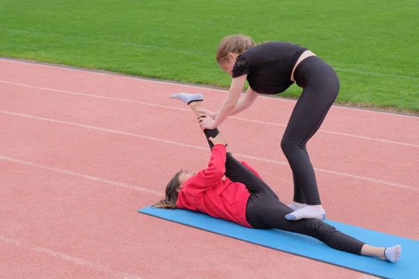 Dívčí trenér pomáhá roztáhat svaly. Roztahuje se pro ženu. Trénink před halou. Letní. — Stock fotografie