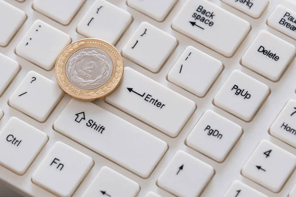 Two pesos close-up. A silver coin with a gold border lies on the keyboard with the Latin alphabet. Selling on the Internet. Buy cryptocurrency.