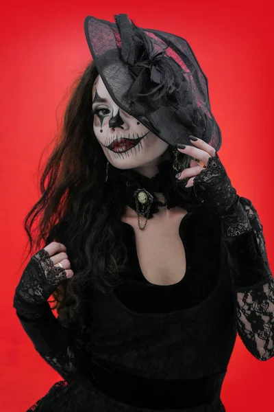 Portrait of a young brunette with make-up in the style of Halloween in black clothes and hat. Horrible girl with scary mouth and eyes, extreme body-art. The image of a witch or an evil clown. — Stock Photo, Image