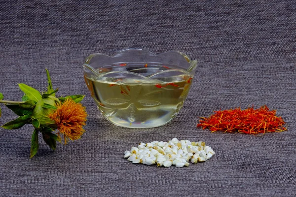 Safflower for cosmetics and spices to food. Saffron flowers and seeds in a pile on the table. Cosmetic vegetable oil in a glass Cup.