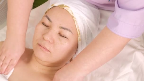美容师擦拭皮肤 清洁一个亚洲女孩颈部和脸上的藻类化妆品面罩的残存 美容中心女性手和脸的特写镜头 美容程序 — 图库视频影像