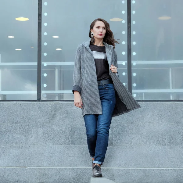 Beautiful girl walks through the city. Stylish brunette in a coat and jeans goes ahead. Spring or autumn. Fashion advertising demi-season clothing. Young female model posing for photo in the street.