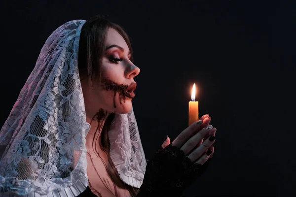 Krásná dívka oblečená jako hrozná jeptiška má zapálenou svíčku. Ženský portrét s Halloweenskou make-upem. Představa hororního plakátu nebo pozvání na stranu strachu. Černé pozadí. — Stock fotografie