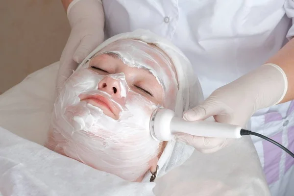 Microcurrent gezichtsmassage. Vrouw op een cosmetologische procedure. Close-up. Hardware cosmetologie. Vrouwelijk gezicht bedekt met witte massage crème. — Stockfoto