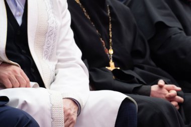 Beyaz elbiseli müslüman bir molla ve siyah cüppe giymiş bir Hıristiyan rahip yan yana oturuyorlar. Dini işbirliği, anlayış, hoşgörü ve dostluk kavramı.
