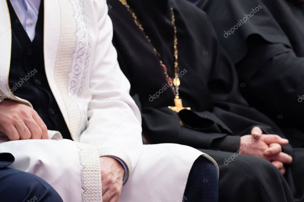 A Muslim mullah in white clothes and a Christian priest in a black cassock are sitting next to each other. The concept of religious cooperation, understanding, tolerance and friendship.