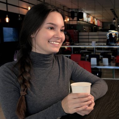 Gülümseyen kız elinde plastik bir fincan çay tutuyor. Genç bir kadın şirkette ya da yalnız bir fincan kahve içerek zaman geçirir. Kare kare. Öğle yemeği